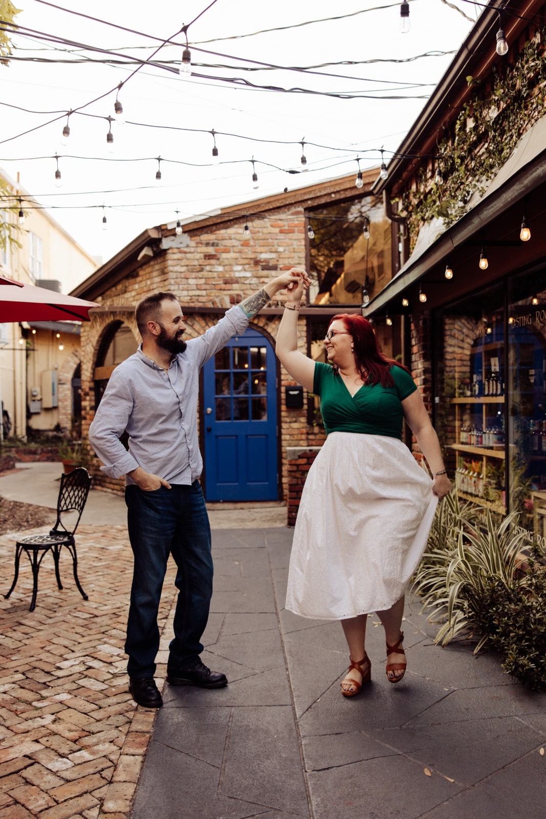 man spins woman in outdoor courtyard with market lighting overheard