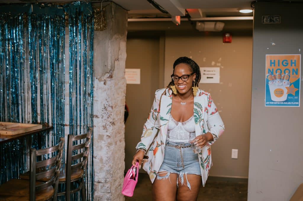 woman with floral print blazer and jeans shorts on walks into room smiling big