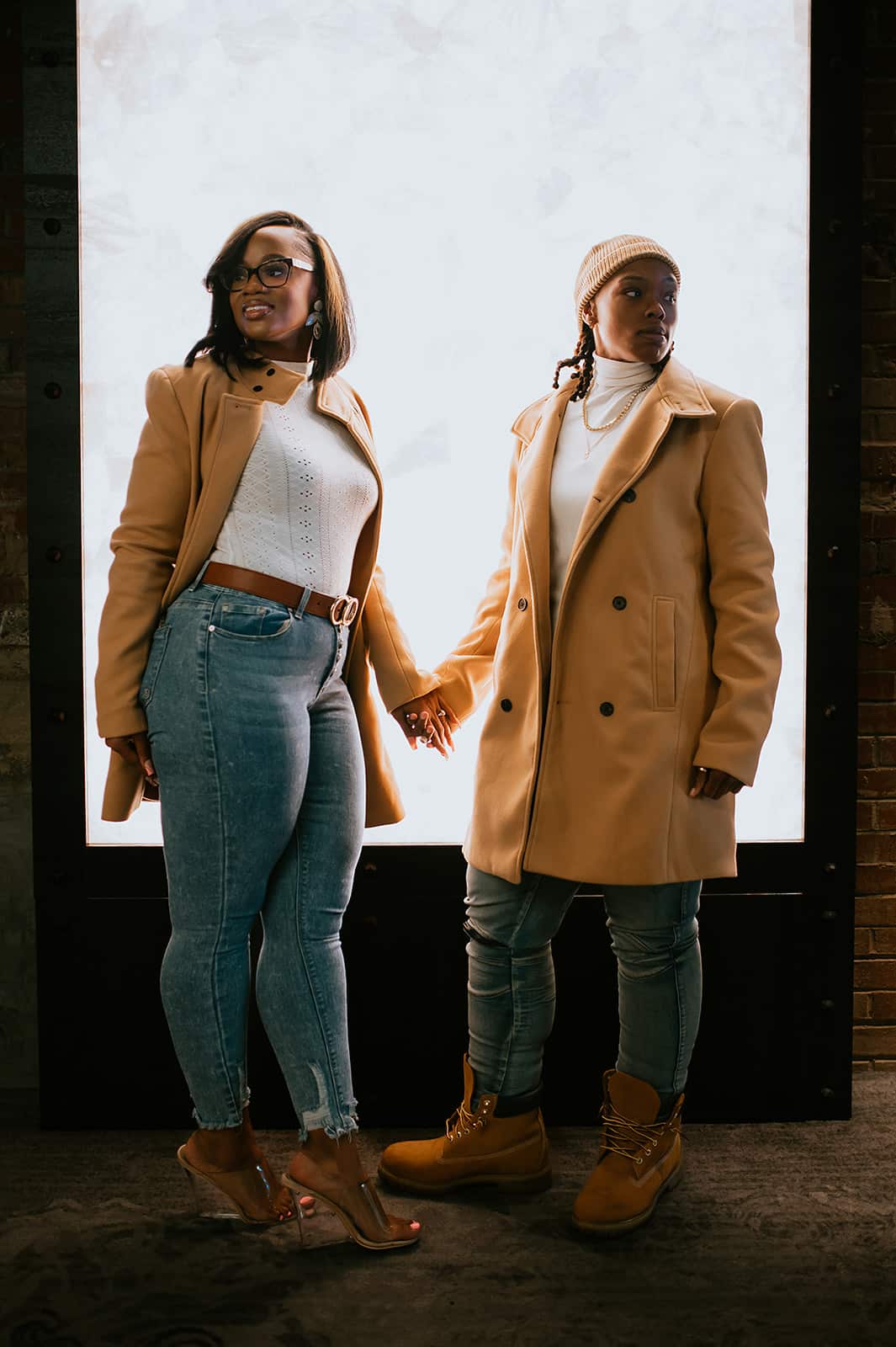 couple with matching tan jackets hold hands with their bodies facing each other but looking opposite ways