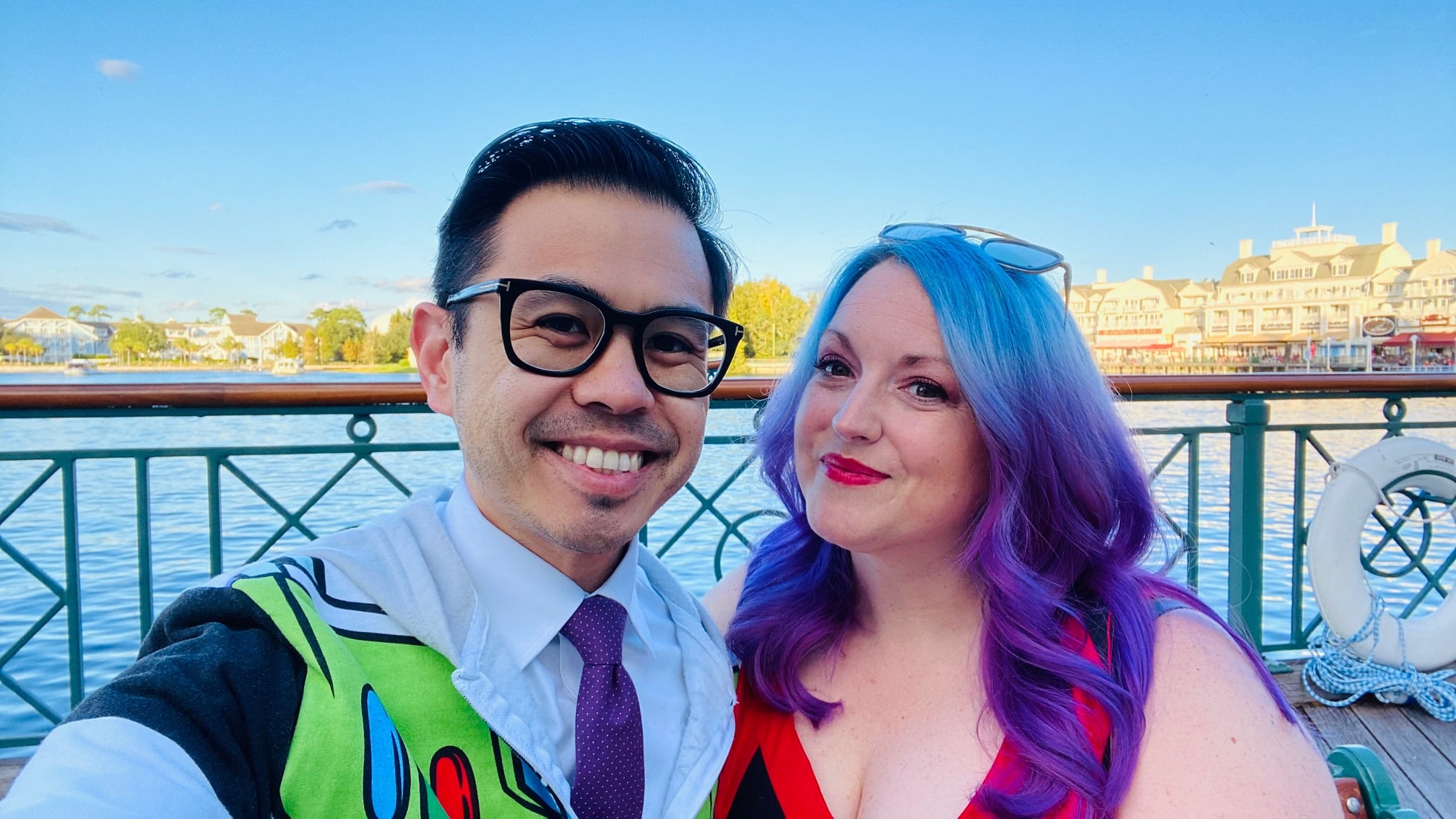 woman with blue and purple hair stands next to man wearing black framed classes smiling