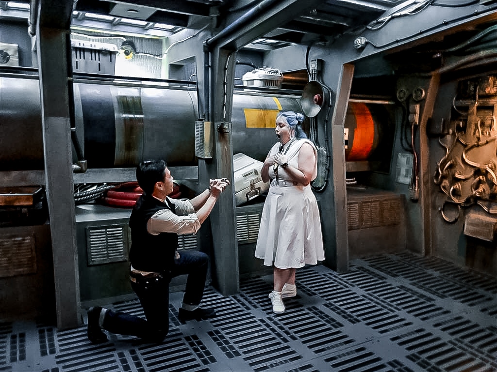 man kneels on one knee in Disney star wars themed area as he proposes to woman