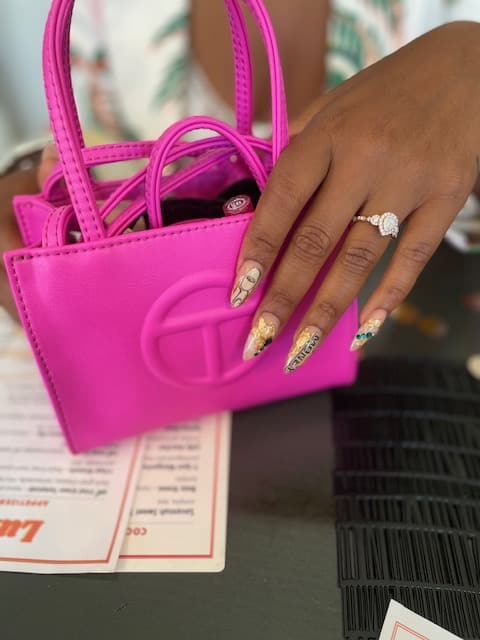 womans hand with long nails and engagement right sitting on bright pink hand bag