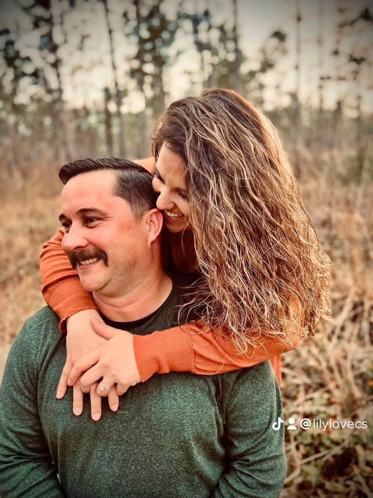couple posed for portrait pictures outside in woodsy area look off to the side while smiling