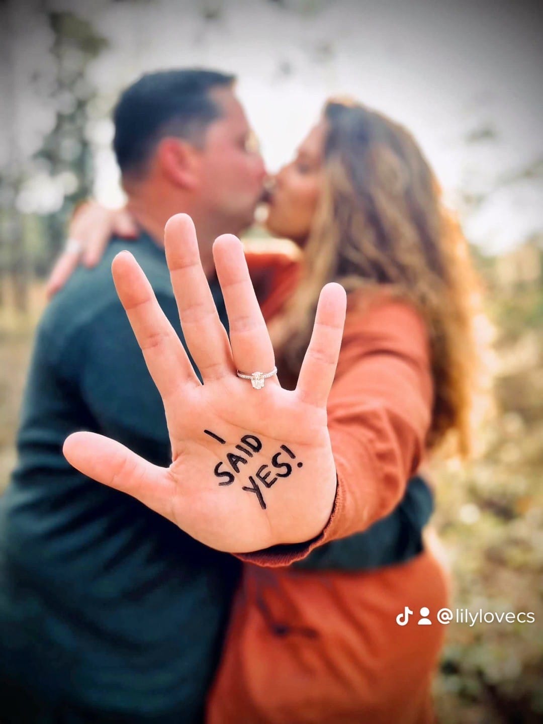 man and woman kiss in picture while woman holds hand towards the camera with "i said yes" written on the palm of her hand