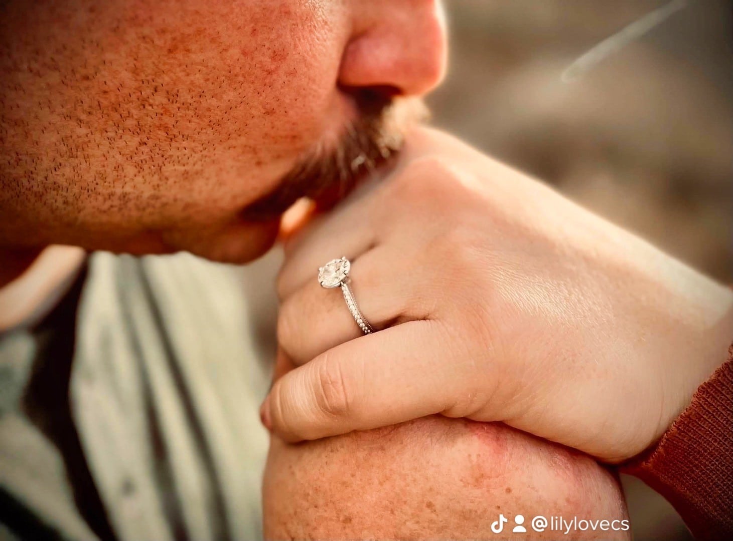 man holds womans hand with engagement ring on it while kissing it