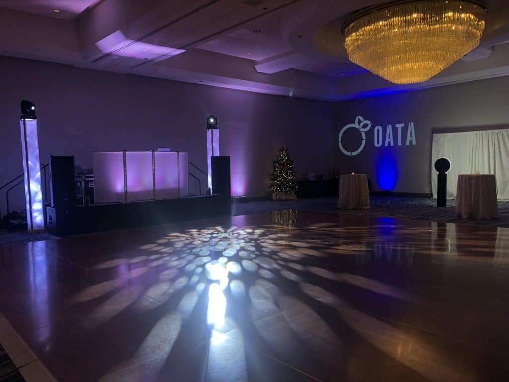 Zoomed out view of the event space, dance floor with soft purple up lighting and a DJ booth set up to the back left, photo booth set up to the far right, wide open dance floor, Dash of Class Platinum, Orlando, FL
