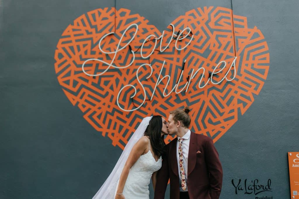 Wedding Couple kissing under a mural and sign that was a red heart with a symmetrical design, a lighted sign that said Love Shines, Orlando, FL