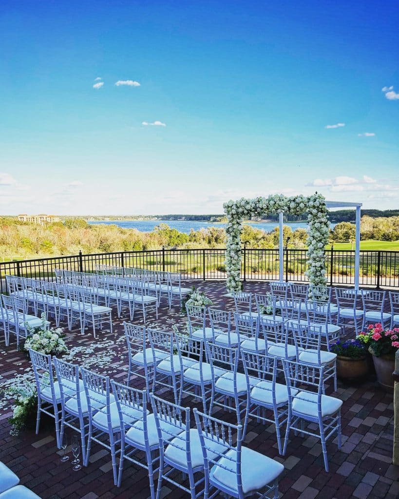 Outdoor wedding ceremony with white chairs in rows with a center aisle, alter adorned with white flowers, overlooking a field and water in the background, Orlando, FL