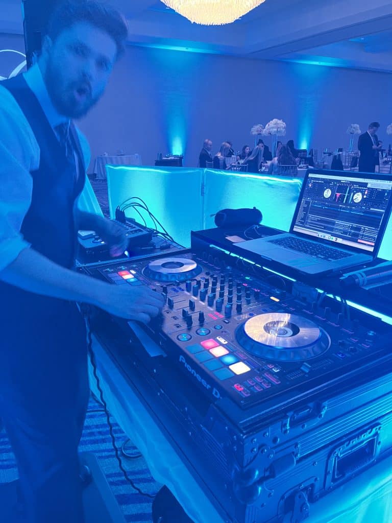 A DJ is playing music for the guests at an event with blue uplighting, Dash of Class Platinum, Orlando, FL
