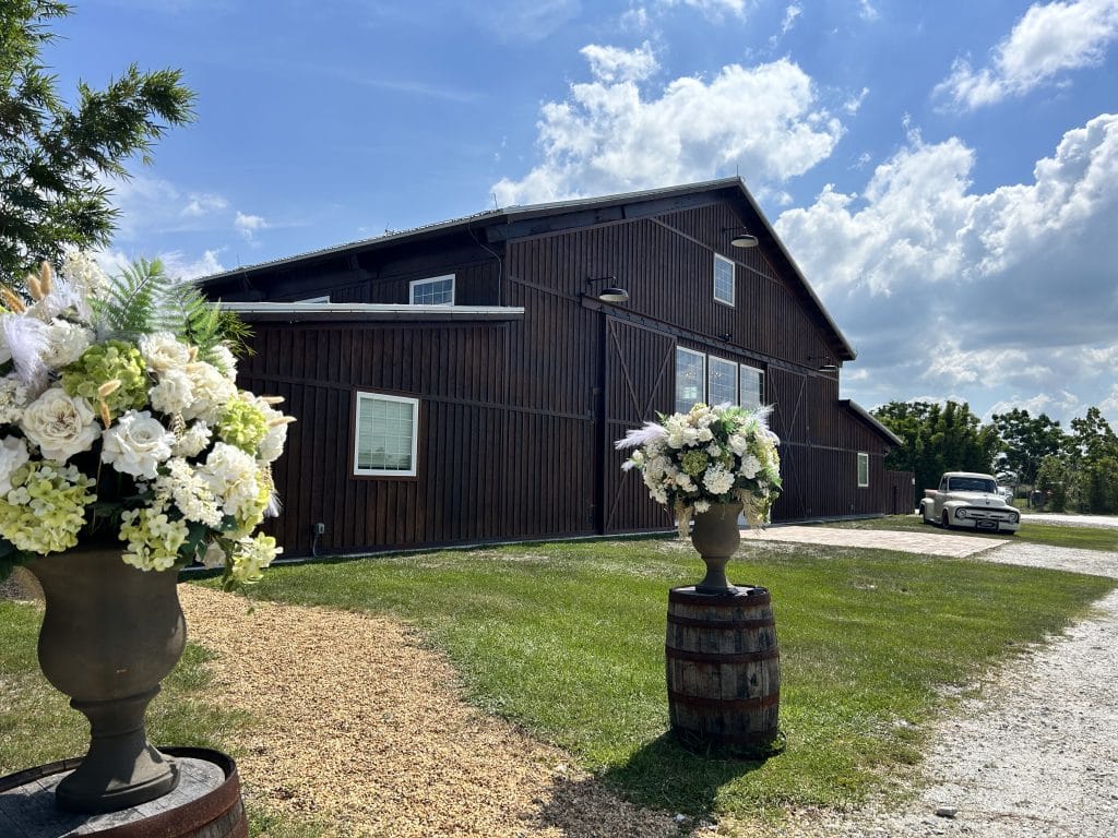 outdoor location with a brown barn in the background, white flowers with greenery in vases at the start of the driveway, Orlando, FL