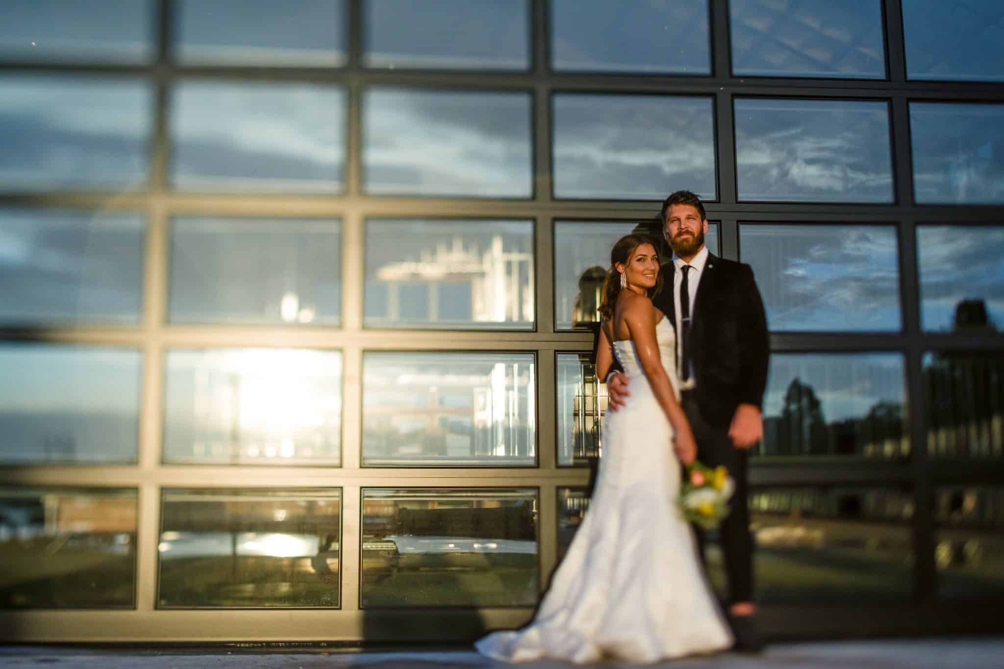 Bride and groom posing in from of a glass wall of a building, near sunset with a reflection on the glass, Lavender on the Lake, Orlando, FL
