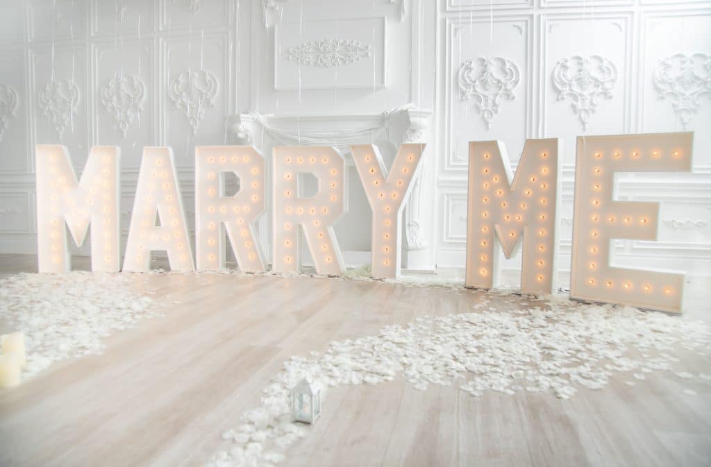 MARRY ME letters spelled out and lit up on the light colored hard wood floors with white flower petals all around, Orlando Marquee & Decor, Central FL