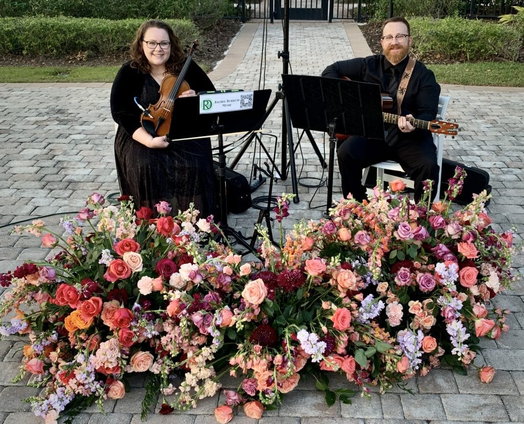Rachel Durrum Music LLC, duo of musicians, one on violin, one on guitar, playing with large flower arrangements in front, Orlando, FL