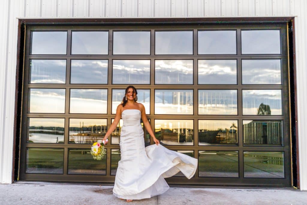 Bride showing off her white wedding dress in front of a glass wall that doubles as a garage door, the rest of the property reflected on the glass, Lavender on the Lake, Orlando, Fl