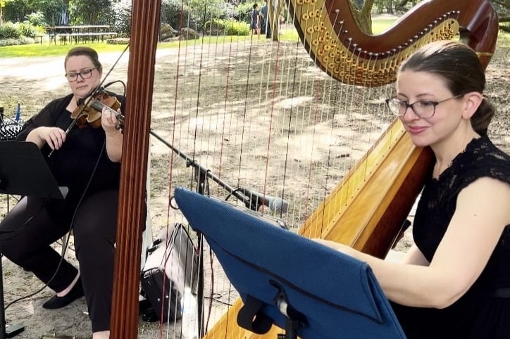 Two members of the musical group Rachel Durrum Music LLC are performing for a ceremony, one on violin and the other on the harp, outdoors, Orlando, FL