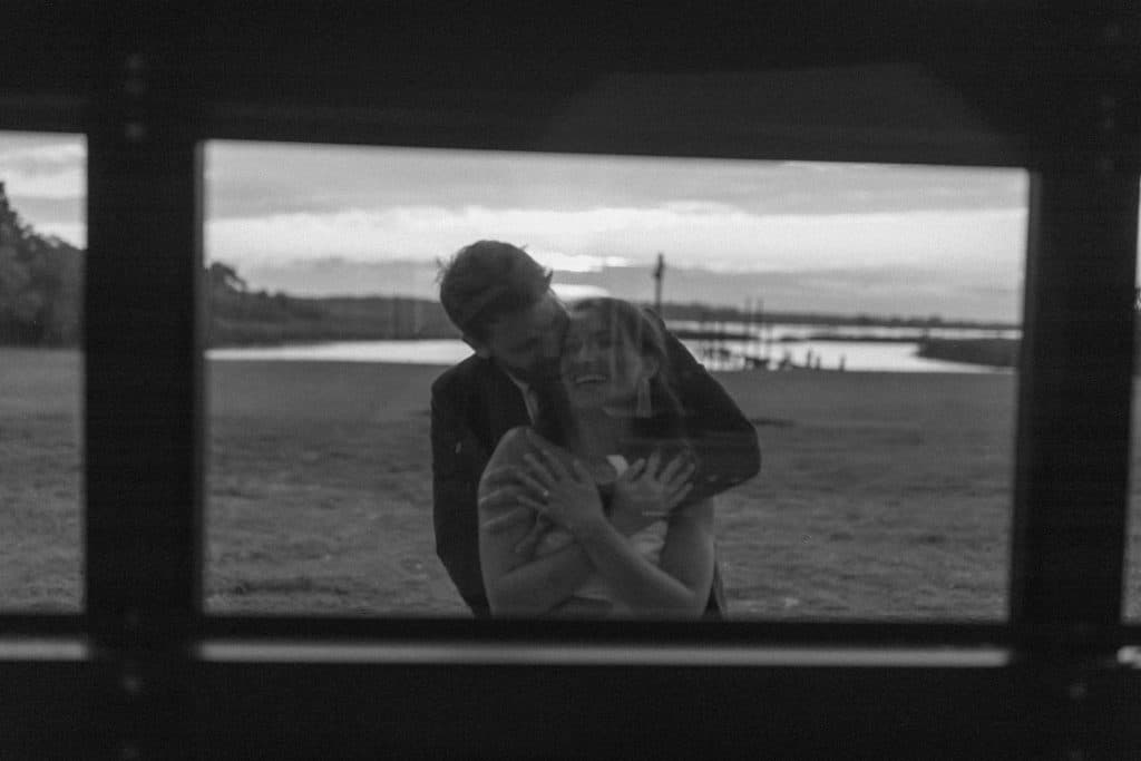A black and white photo of a wedding couple on the outside of the garage door glass wall, photo taken from inside, lake in the background, Lavender on the Lake, Orlando, FL