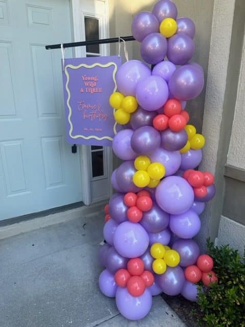 Balloon column dated with two shades of purple, yellow and pink balloons, accompanying a purple sign for the occasion, Orlando Marquee & Decor, Central FL