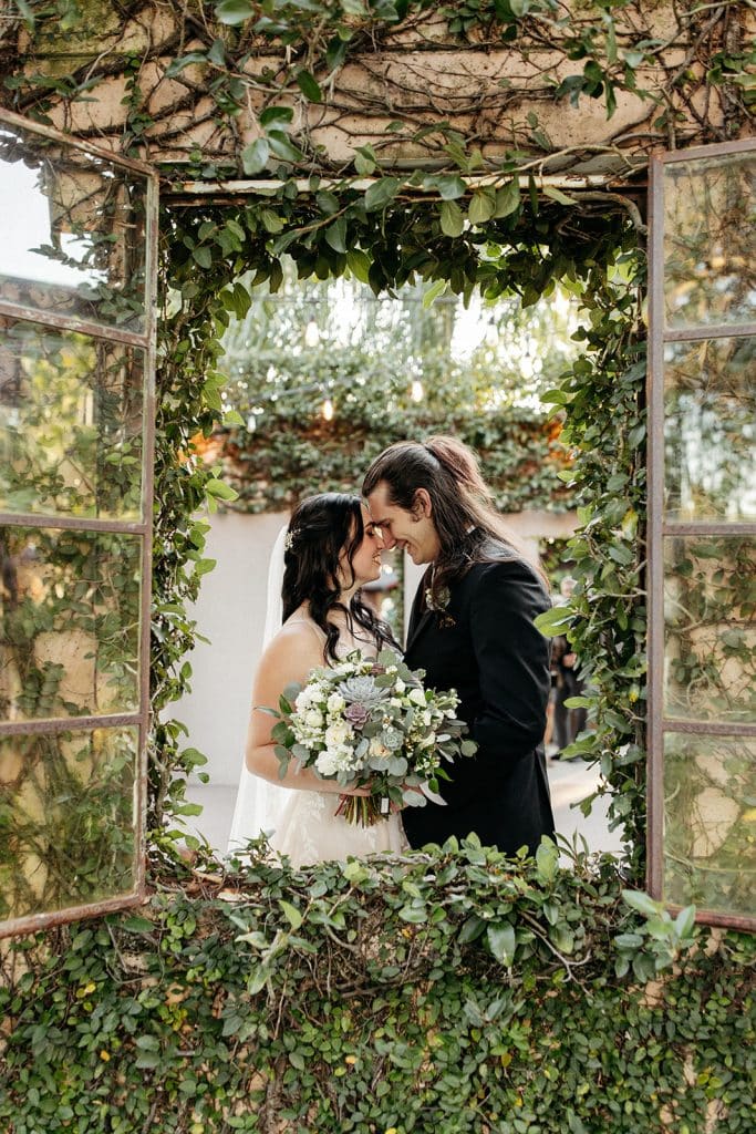 Wedding couple standing close, almost kissing, framed in a window with lots of greenery around, Serenity Events, Orlando, FL