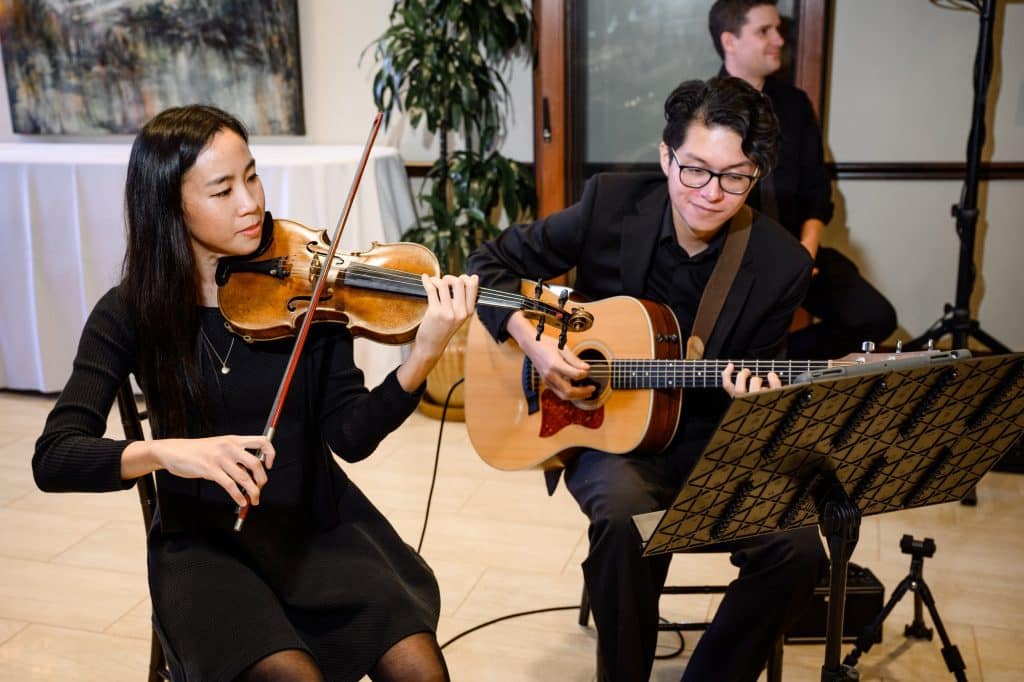 violinist and guitarist sit playing wearing all black
