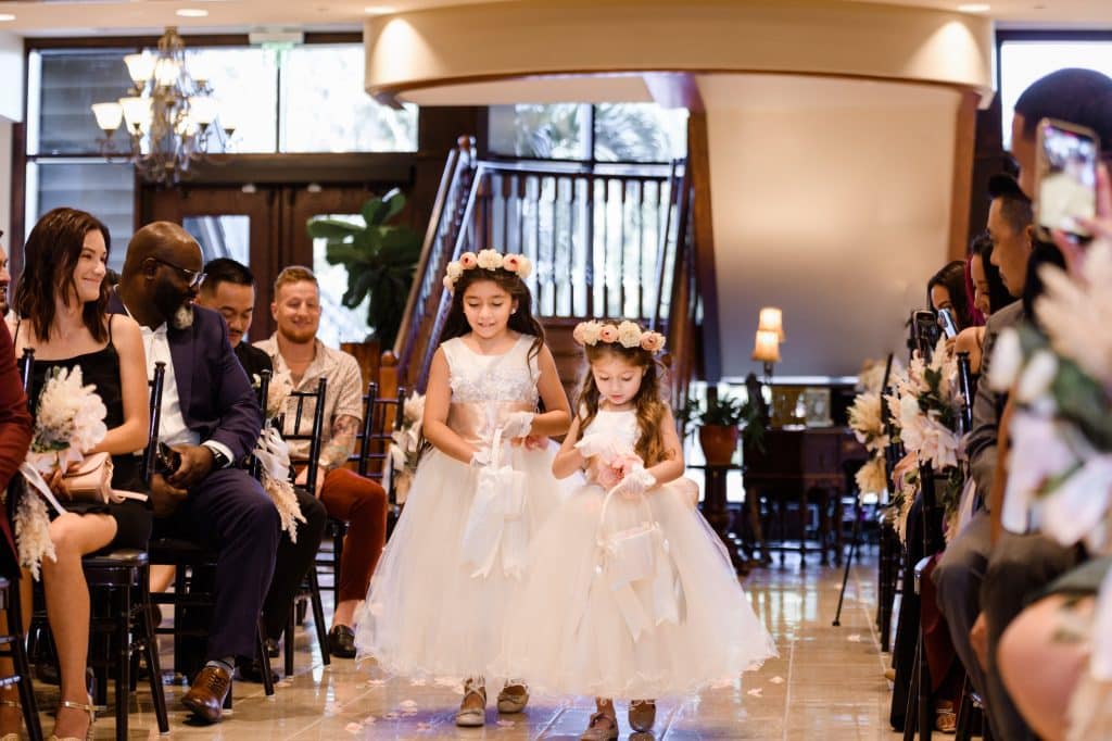 two flower girls wearing white dresses and flower crowns walk down the aisle throwing petals