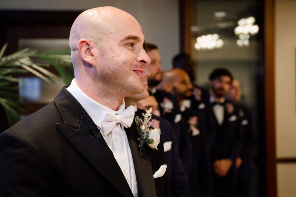 groom looks towards aisle as bride walks down with groomsmen behidn him