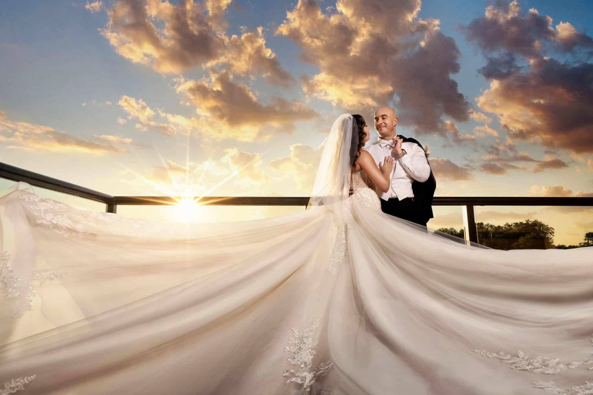 husband and wife on wedding day pose for dramatic picture outside with sun and clouds
