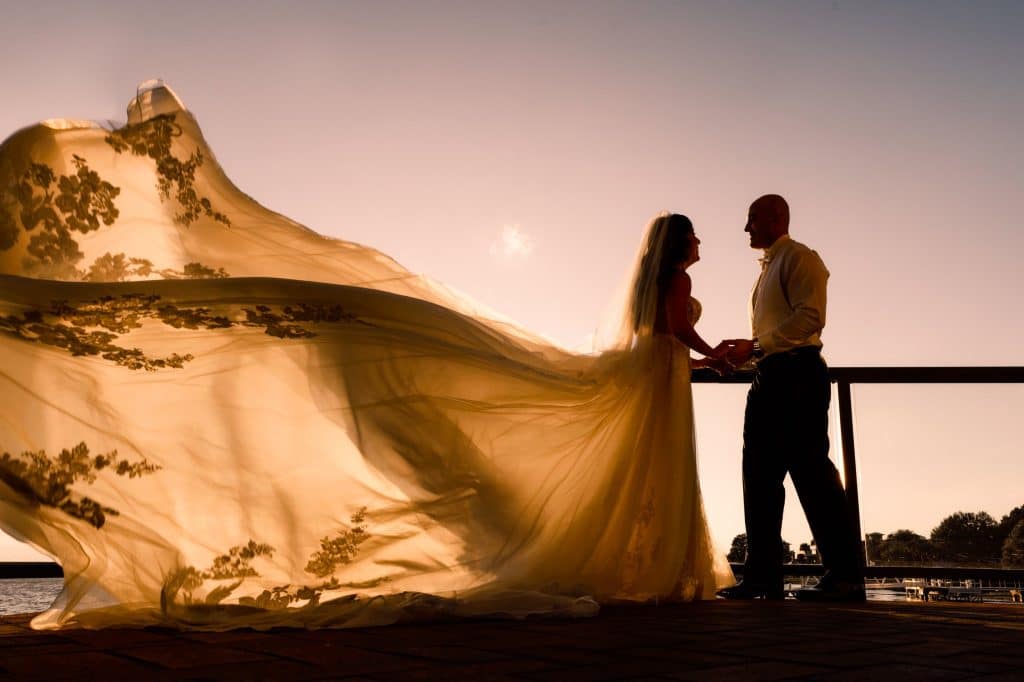 sunset picture with brides dress floating in the air standing next to groom