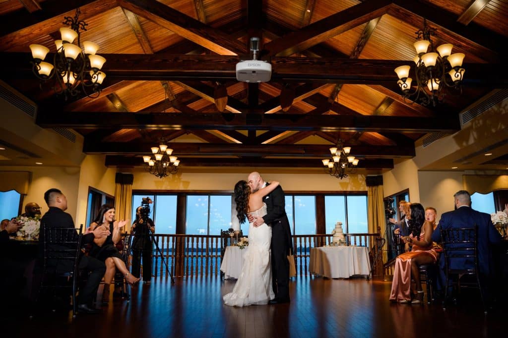 husband and wife first dance on wedding day in front of windows overlooking water