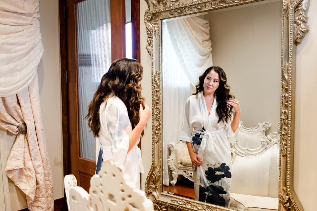 woman in white robe looks at self in mirror
