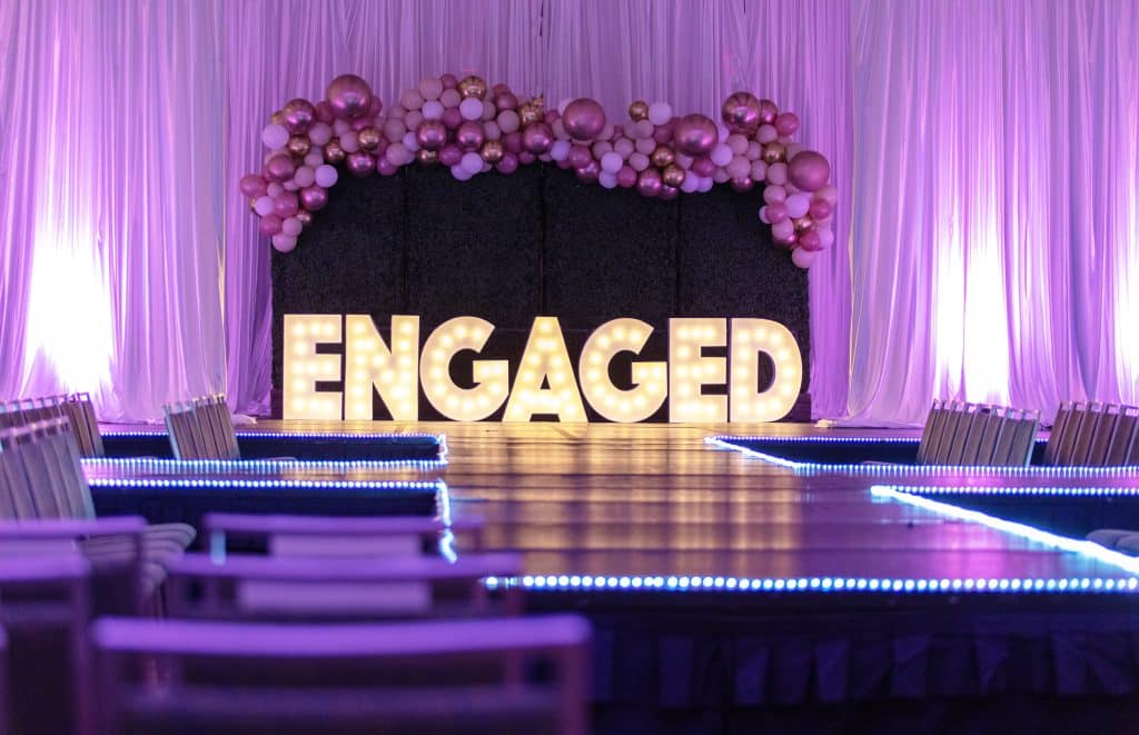 Stage set up with the word ENGAGED spelled out in lighted letters with a purple backdrop, Orlando Marquee & Decor, Central FL