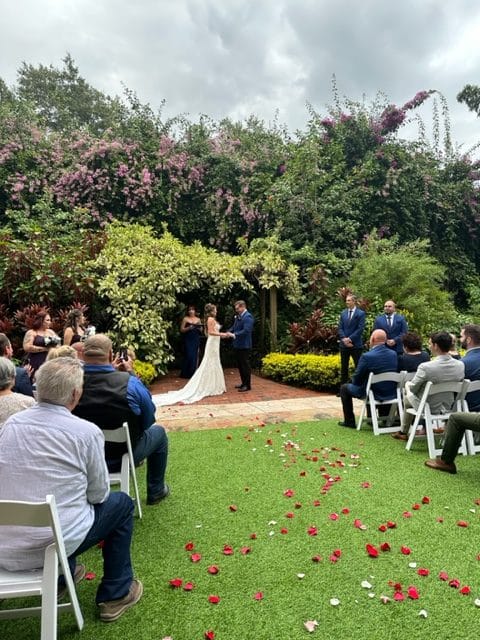 outdoor wedding ceremony, rose petals on the ground, wedding guests look on as the ceremony is happening, beautiful greenery in the background, One Night Only, Orlando, FL