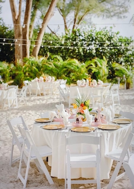 round tables, set for 8 at each, white tablecloths, gold chargers, flower centerpieces, string lights hung from above, greenery in the background, Orlando, FL