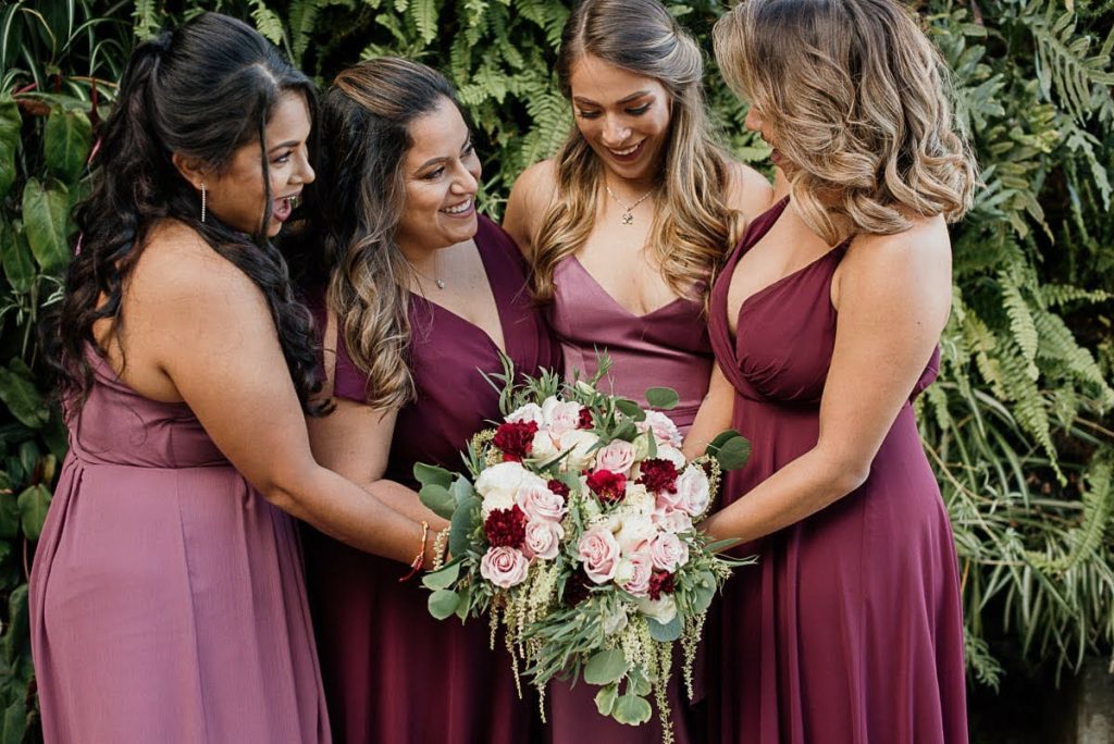 Bridesmaids in dresses in shades of pink and maroon, all holding a bouquet of flowers together in a circle, Orlando, FL