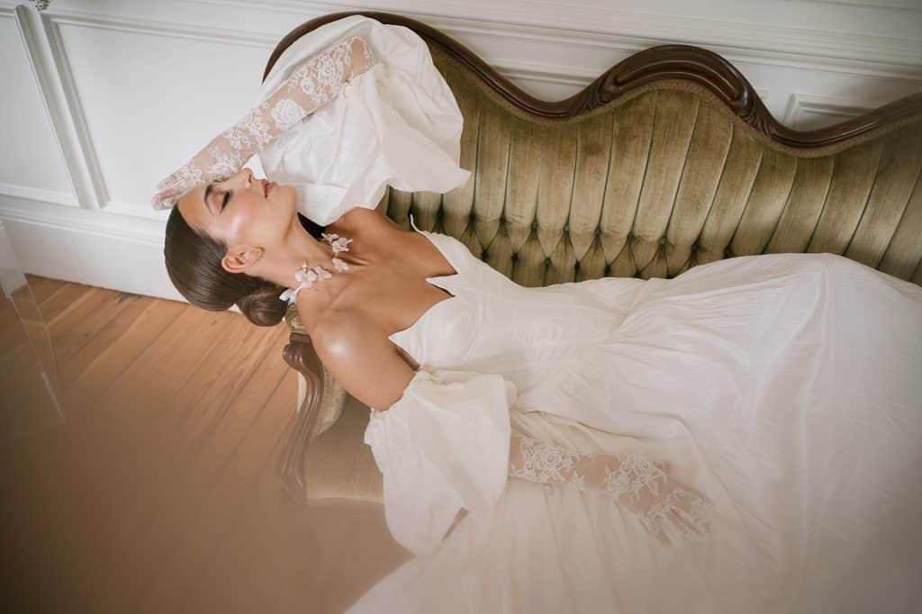 Bride laying on an antique olive green sofa in her wedding gown, facing the ceiling, APG Beauty, Central FL