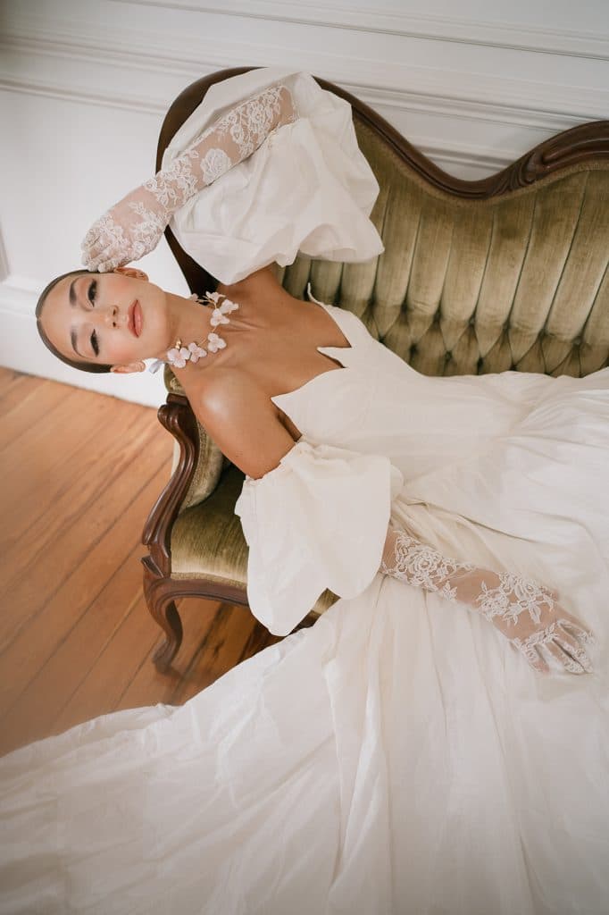 Bride laying on an antique olive green sofa in her wedding gown, facing the camera, APG Beauty, Central FL
