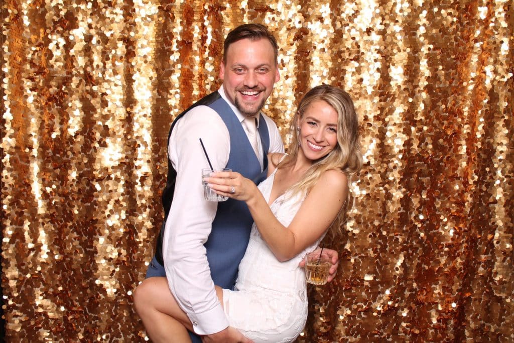 Man and woman posing in front of a golden sequin curtain holding cocktails