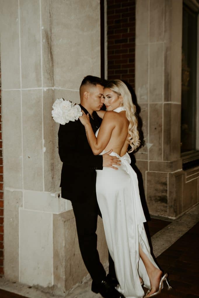 Bride and Groom leaning against a building in an embrace in their wedding attire, Central FL