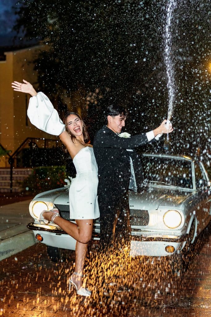 Wedding Couple celebrating with a bottle of champagne by their car, before leaving their reception, Central FL