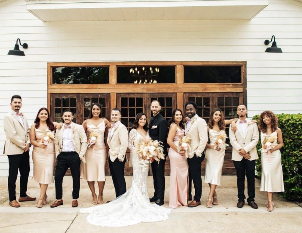 Wedding party posing in front of the venue, posing to the camera, men wearing tan jackets and black pants, women in varying shades of pink and tan dresses, Central FL