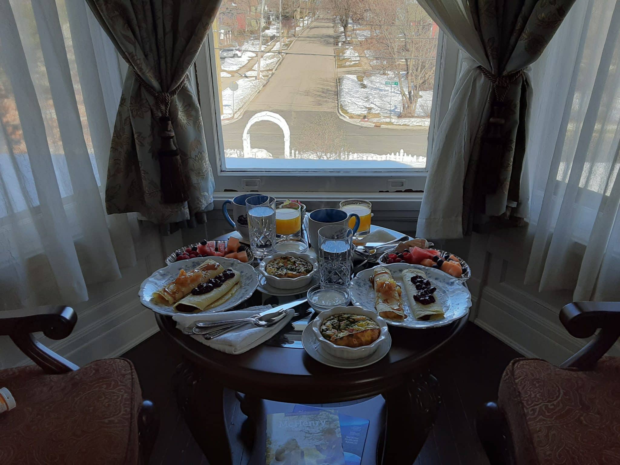 table setup in front of window with breakfast for two covering the top of it and two chairs at the table