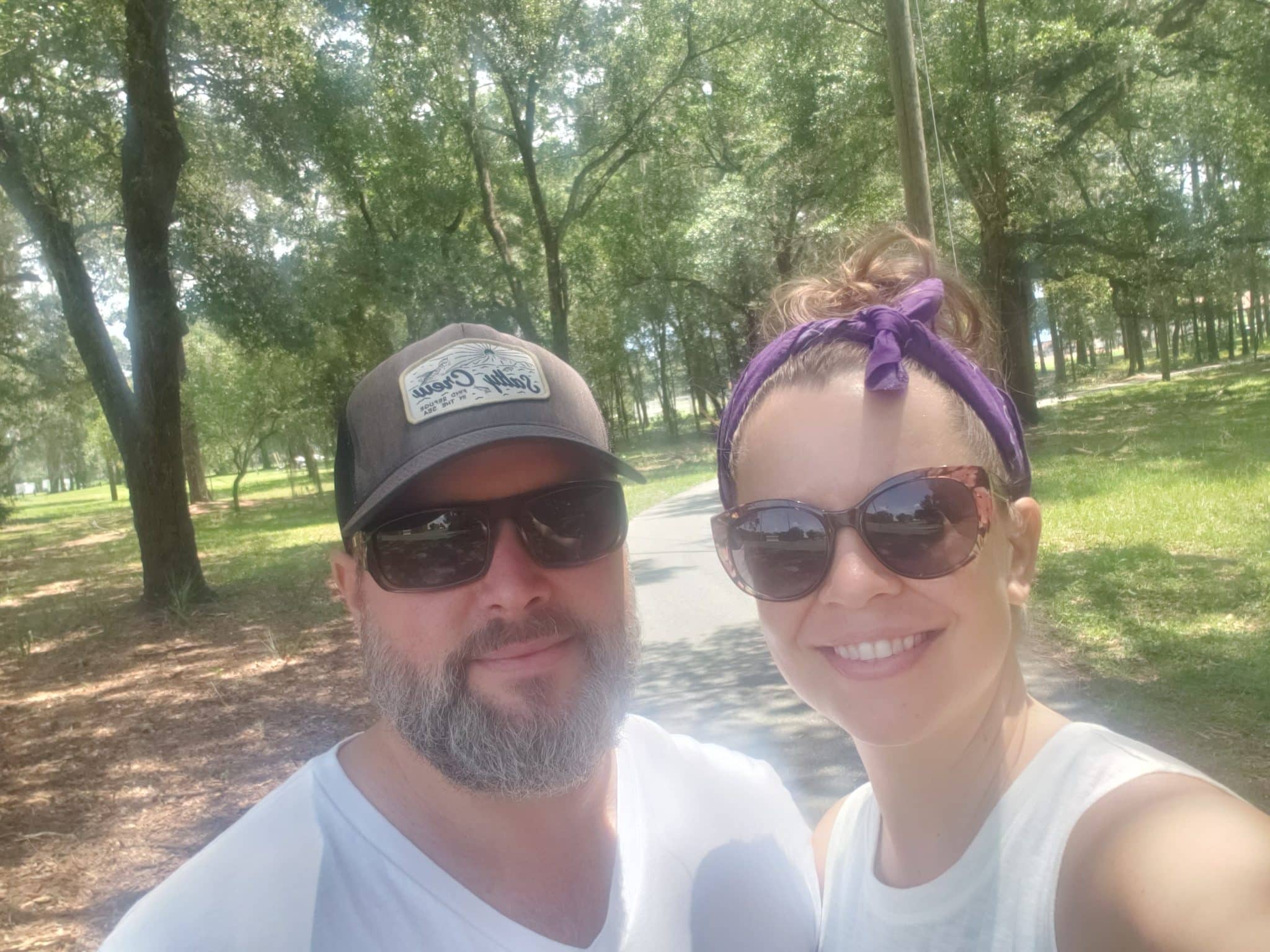 man and woman wearing white shirts and sunglasses out doors take selfie on nature path