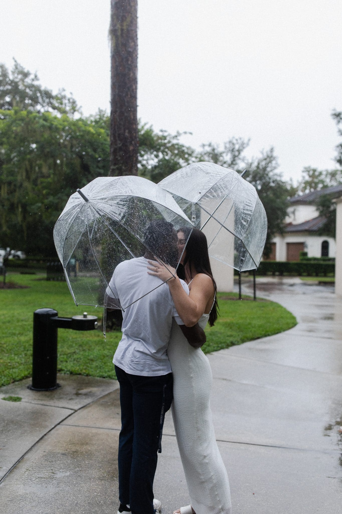 couple stands outside kissingwhile holding clear umbrellas
