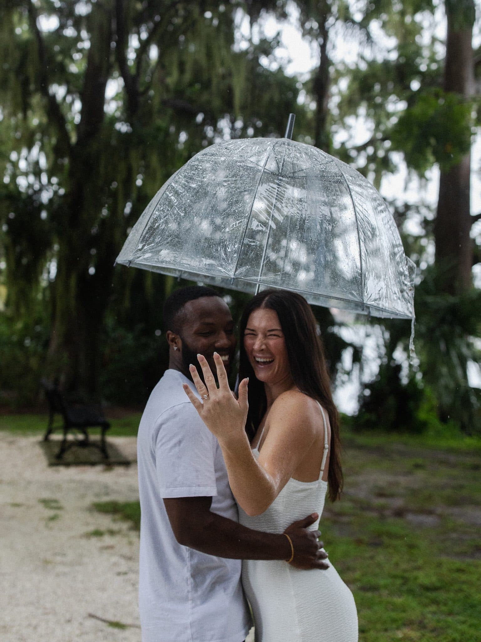 couple pose together for picture outside in park with clear umbrella