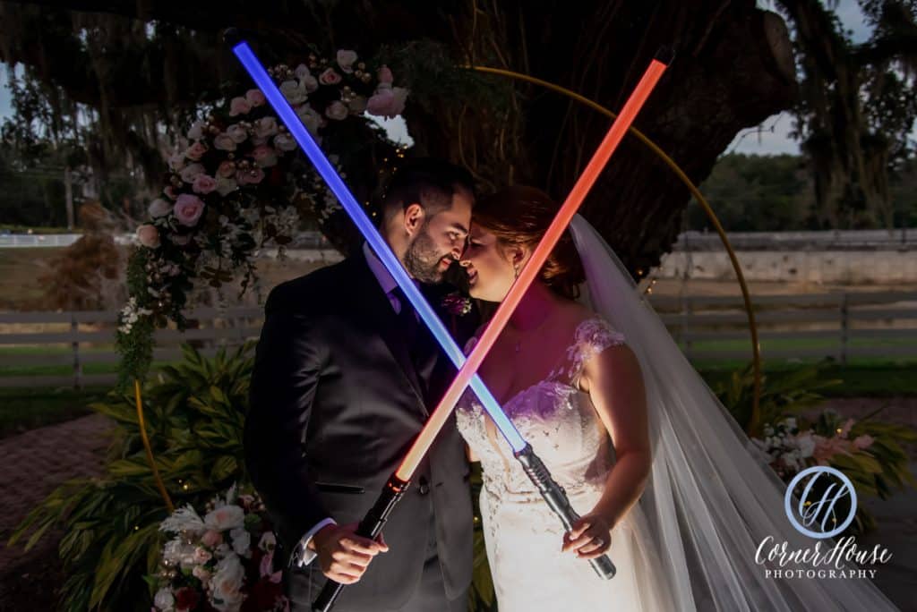 bride and groom holding their light sabers, in an X formation, lit up at night in front of their round pergola, P.S. I Love You Weddings & Events, Orlando, FL