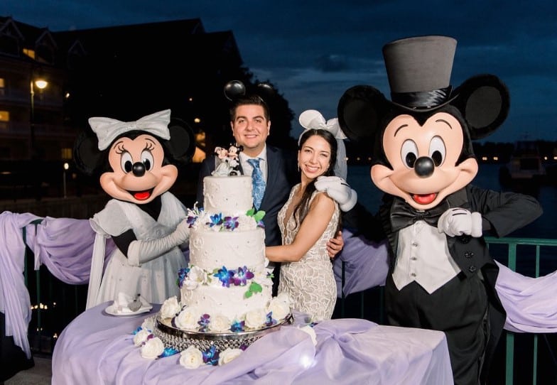 Bride and groom hanging out with Mickey and Minnie Mouse in their best wedding attire, large three tiered wedding cake on the table, light purple tablecloths, P.S. I Love You Weddings & Events, Orlando, FL