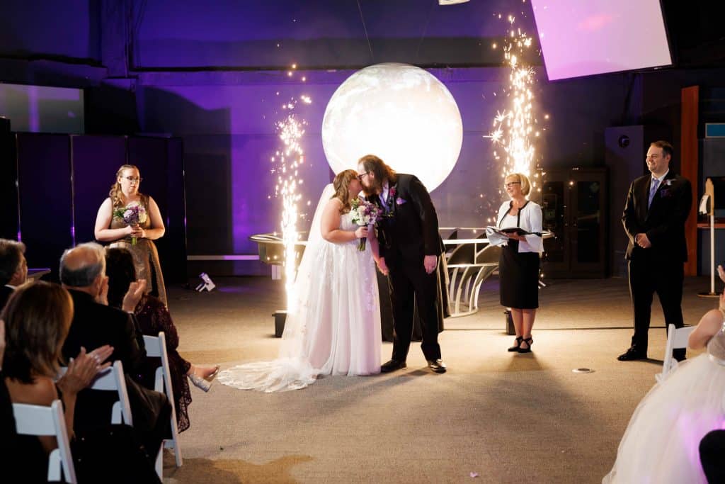 indoor wedding ceremony with a set of sparklers in the background, with a large moon, guests watching as the couple kisses, Orlando, FL
