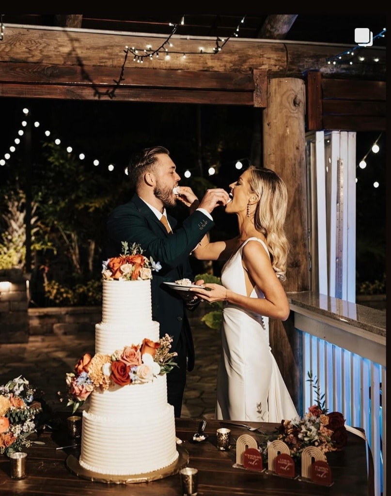 bride and groom feeding each other cake, four tiered wedding cake, colorful flowers adorning the sides, central fl