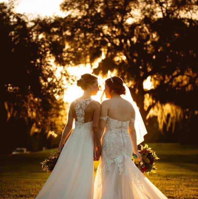 both brides walking together, hand in hand, towards the sunset, wearing their wedding gowns, carrying their bouquets, Orlando, FL