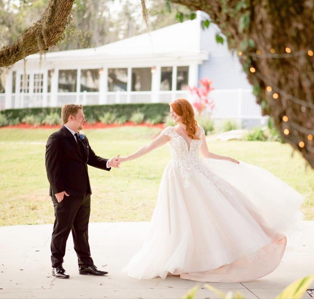 bride and groom outdoors, holding hands as they walk towards each other, venue in the background, tree in the foreground, P.S. I Love You Weddings & Events, Orlando, FL