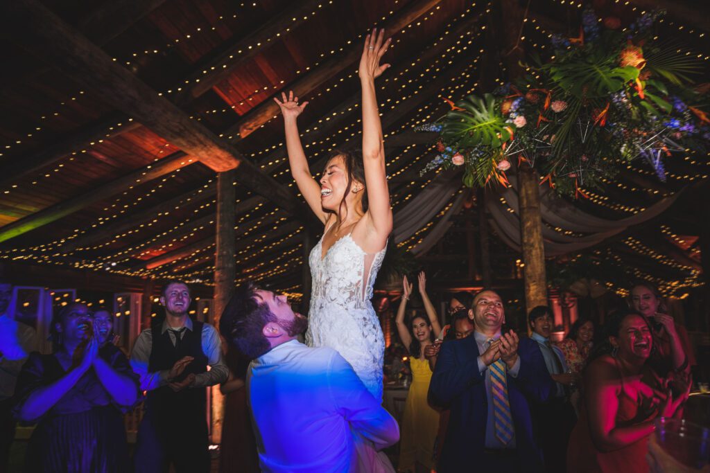 groom lifting his bride on the dance floor, guests celebrating, colored lights on the ceiling, paradise cove, central fl